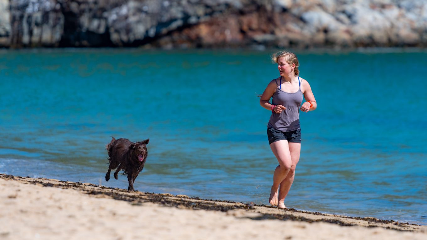woman running on beach with dog